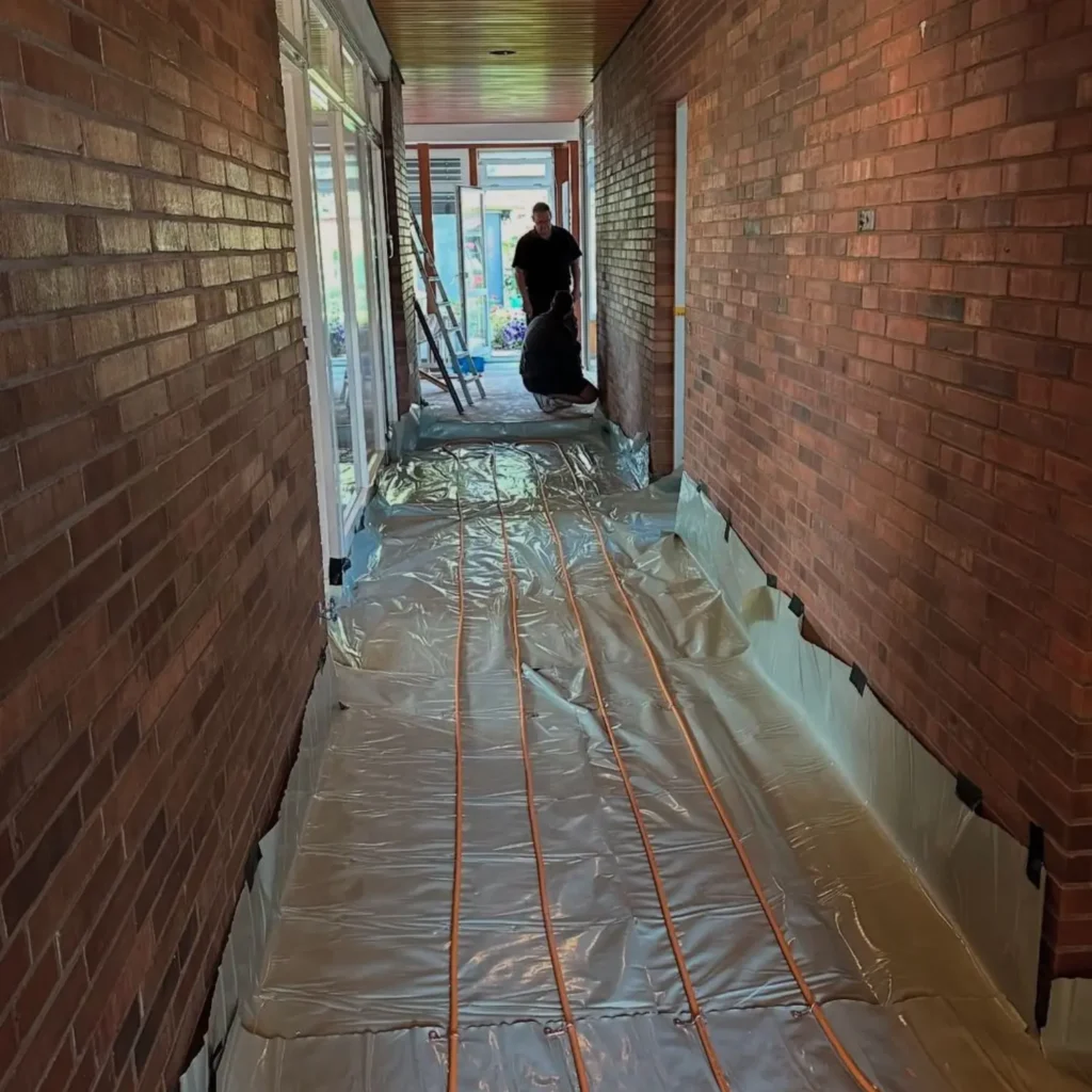Hallway renovation in Zurich before works, with exposed underfloor heating installation and brick walls.