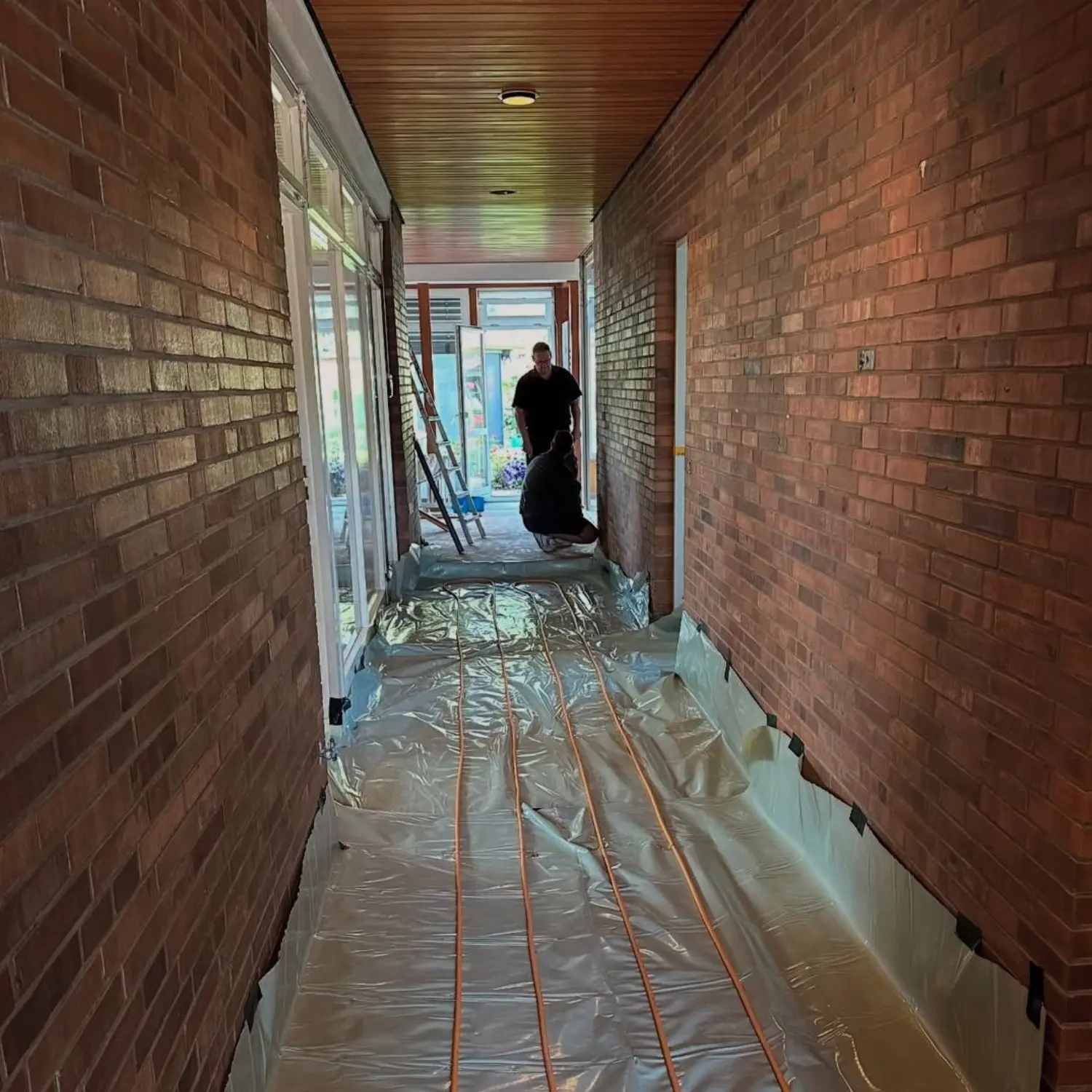 Flur Renovation in Zürich vor den Arbeiten mit sichtbarer Fußbodenheizung und unverputzten Backsteinwänden.