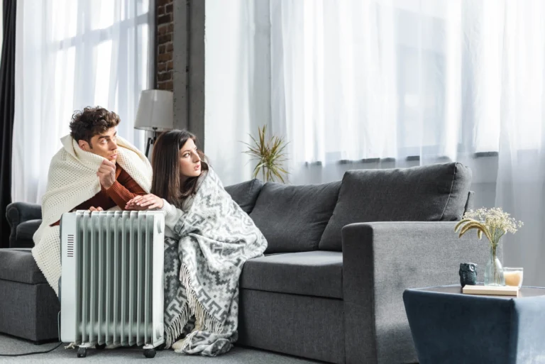 Young couple covered with blankets sitting by a heater in a rental apartment in Zurich during winter