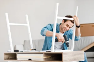 Man assembling flat-pack furniture with a power drill in an apartment, representing IKEA furniture assembly in Zurich